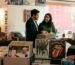 Fotografía de estilo editorial y analógico del interior de una disquería boutique con iluminación cálida. En primer plano, varias cajas metálicas y de madera exhiben discos de vinilo, destacando portadas de artistas como The Rolling Stones y Kiss. A la izquierda, sobre un mueble de madera oscura, se aprecia una tornamesa junto a una lámpara de mesa con acabado en cobre y una taza de café de cerámica. Al fondo, pegados en una columna blanca, se observan pósteres de música en blanco y negro y el texto vertical "VIVE LA EXPERIENCIA". Tres personas con vestimenta casual exploran los discos y conversan de manera natural en un ambiente acogedor y comunitario.