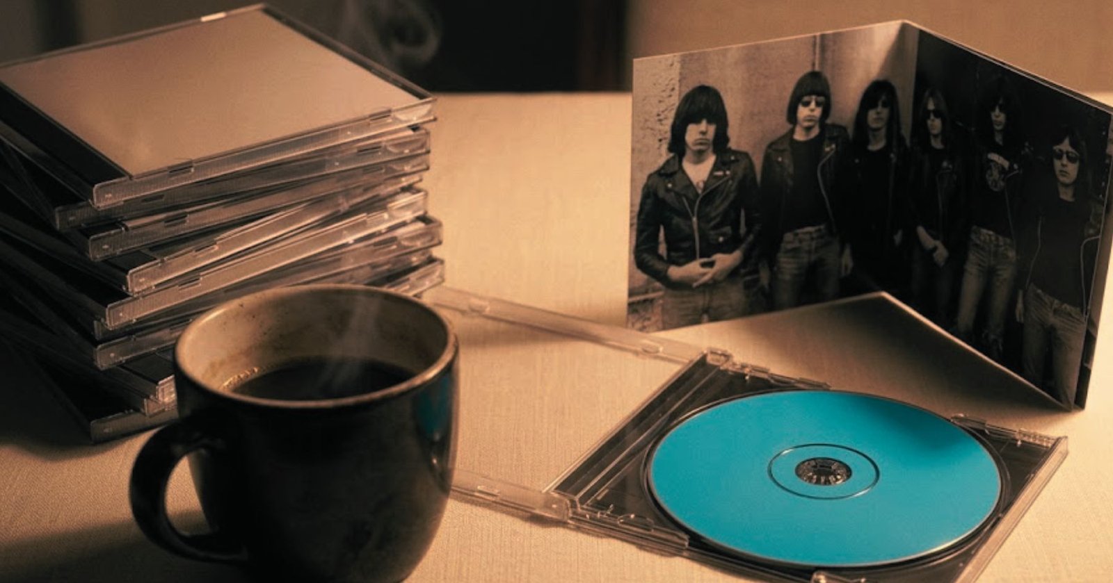 CDs apilados junto a una taza de café en una mesa cálida con estética nostálgica