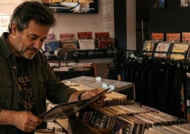 Padre melómano revisando discos de vinilo y CDs como posibles regalos del Día del Padre en una disquería cálida