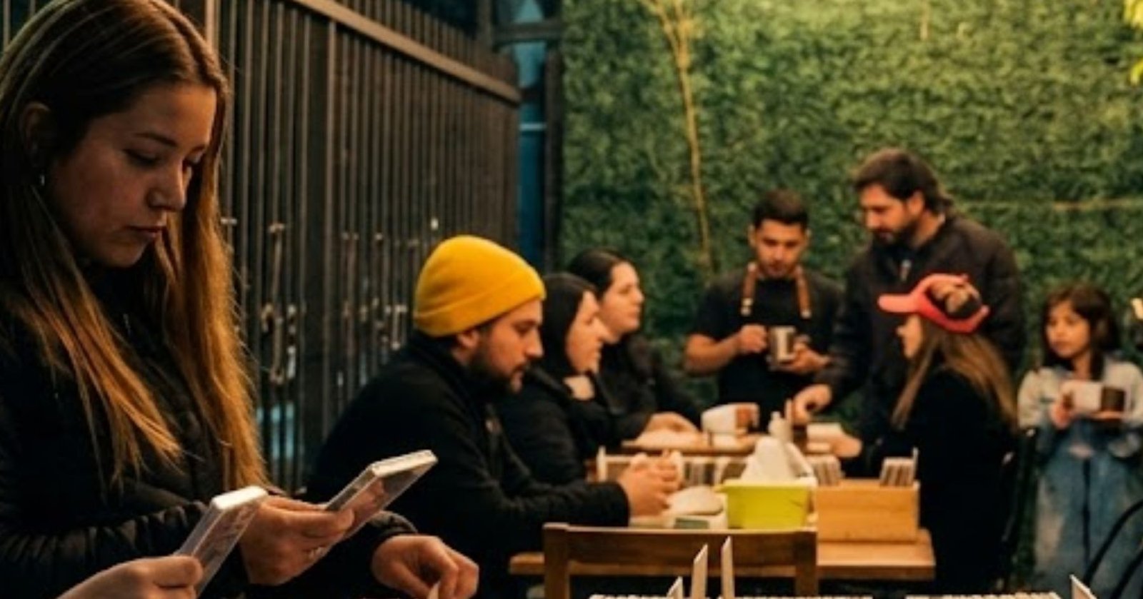 Mesa de feria con varios CDs ordenados, café y personas revisando música en ambiente familiar